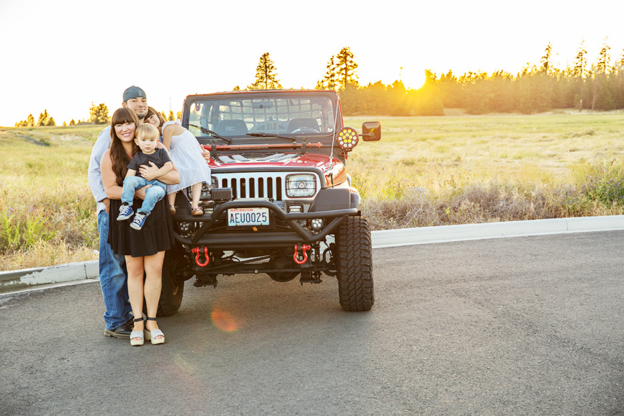 Family posing with their red SUV at sunset