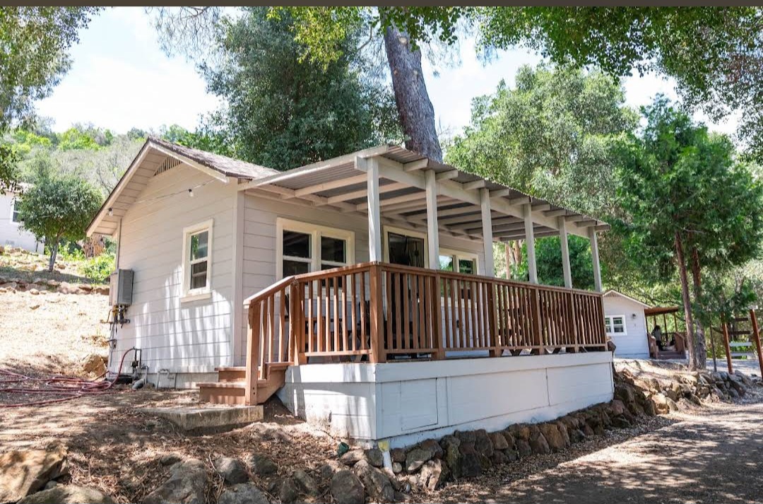 White cottage with wraparound porch and wooden railing shaded by mature oaks at Hideout Mountain