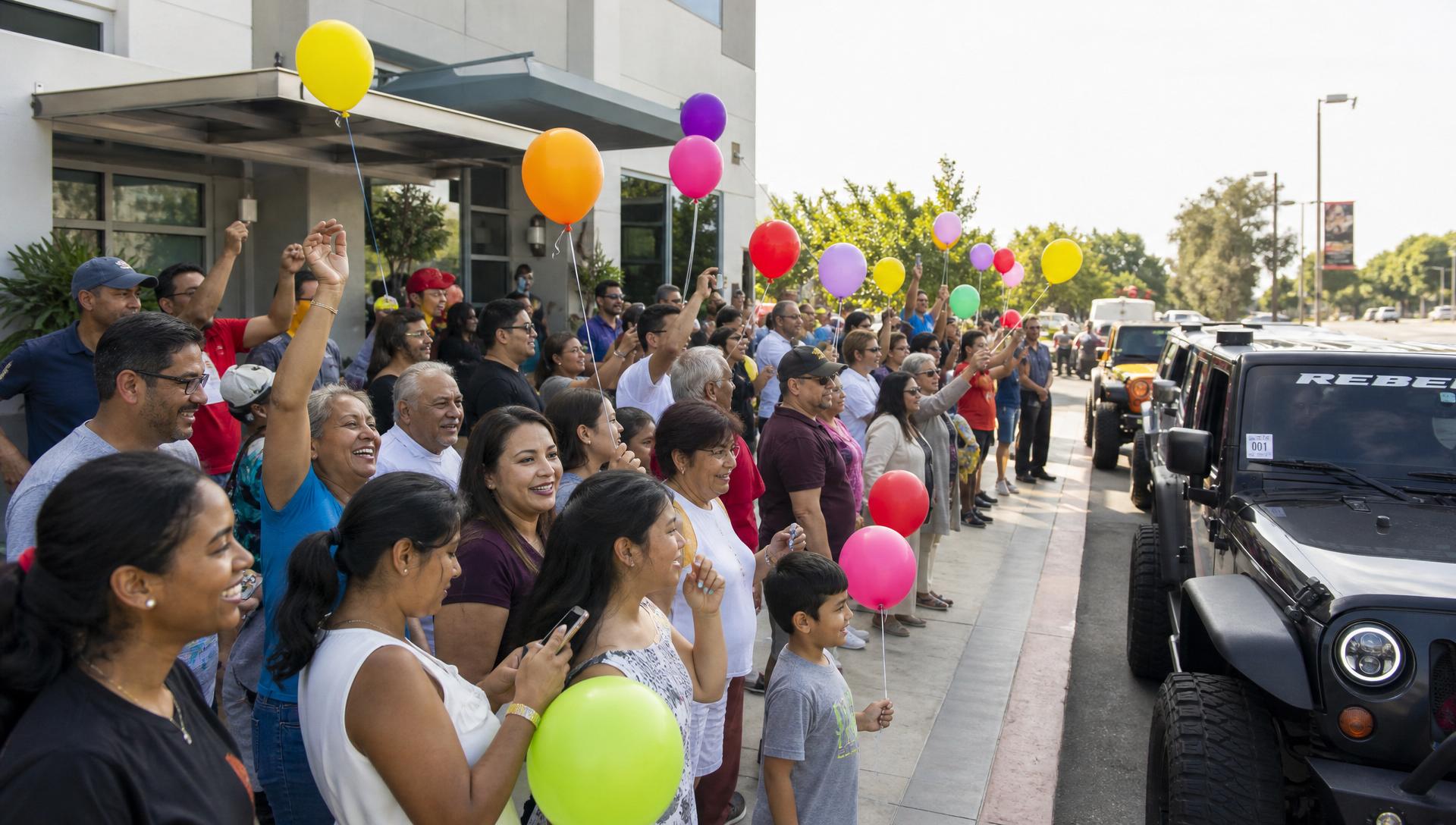 Diverse crowd of families celebrating at the start-line kickoff party with balloons and a mix of cars, SUVs and motorcycles